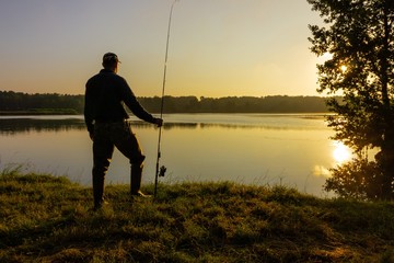Silhouette of angler standing on the shore of the lake during sunrise