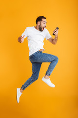 Full length photo of shocked caucasian man having beard wondering and holding cellphone while...