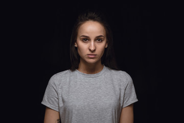 Close up portrait of young woman isolated on black studio background. Photoshot of real emotions of...