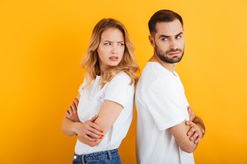 Fototapeta premium Image of upset couple man and woman in basic t-shirts frowning while standing back to back during fight