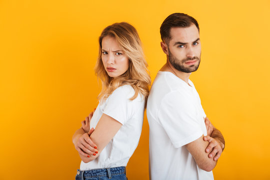 Image of confused couple man and woman in basic t-shirts frowning while standing back to back during fight
