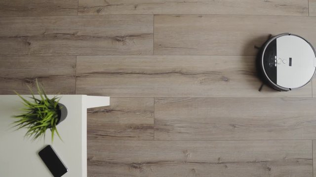 A robotic vacuum cleaner slides across the a modern living room. 4K. top view.