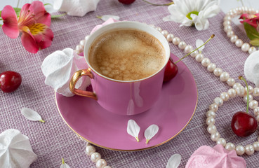Pink cup with fresh aromatic coffee and petals among pearls, flowers and sweets
