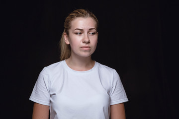 Close up portrait of young woman isolated on black studio background. Photoshot of real emotions of...