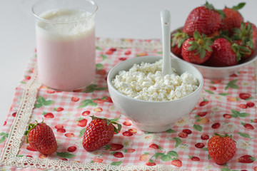 Cottage cheese in a white cup with a spoon, strawberry yogurt and fresh strawberries on a napkin