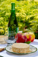 French cheeses collection, piece of fermented cow milk cheese Camembert au Calvados served with French dry apple cider outside in green garden