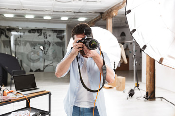 Portrait of young brunette photographer man shooting model with professional camera in studio - obrazy, fototapety, plakaty