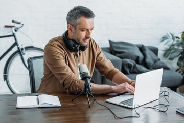 attentive radio host using laptop while sitting at workplace near microphone