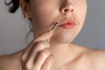 A young woman with a mustache tries to remove the hair over her lip with tweezers. The concept of getting rid of unwanted facial hair. Close up