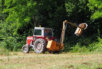 Tractor mounted hydraulic brush cutter at work in a summer day