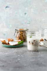 Obraz na płótnie Canvas Homemade layered vegan dessert of baked granola and coconut yogurt in glass jar on gray background