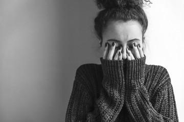 Close up of teenager with depression and bulimia sitting alone in dark room. She covers her face with hands. Mental problems with depression and bulimia. Black nad white photo. - obrazy, fototapety, plakaty