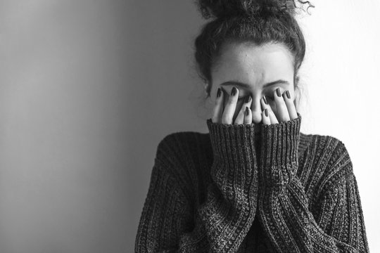 Close up of teenager with depression and bulimia sitting alone in dark room. She covers her face with hands. Mental problems with depression and bulimia. Black nad white photo.