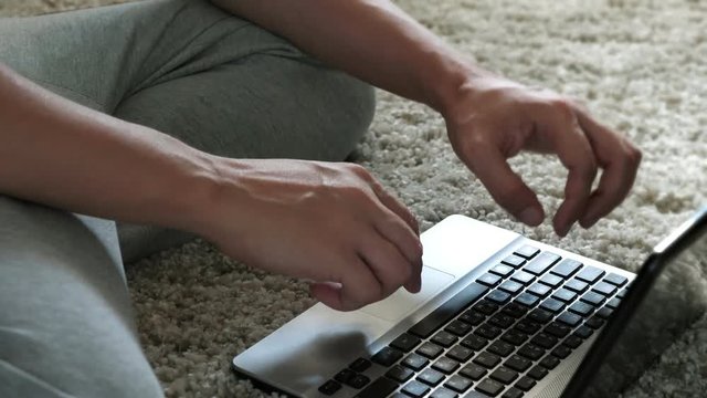 Man sits in home at carpet and using on laptop.