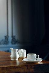 Coffee cup, milk jar, and sugar on wooden table in restaurant interior