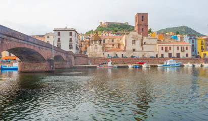 Panorama of the colorful town of Bosa along a river and hills in sunlight in spring