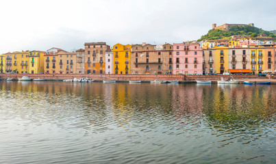 Panorama of the colorful town of Bosa along a river and hills in sunlight in spring