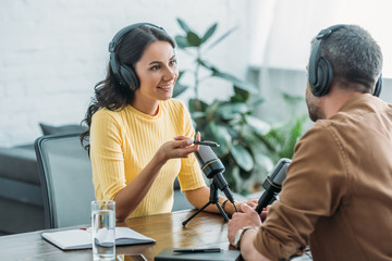 smiling radio host in headphones gesturing while talking to colleague in broadcasting studio