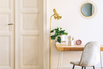 Stylish and elegant home interior with wooden desk, grey velvet chair, design accessories, gold...