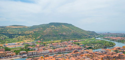 Panorama of the colorful town of Bosa along a river and hills in sunlight in spring