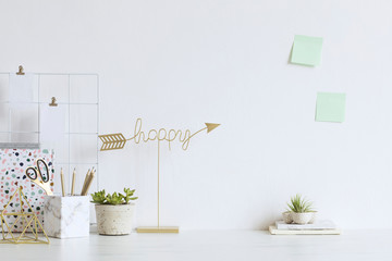 White and stylish home interior with cool office accessories, notes, boxes, pencils and air plant. Gold happy sign. Scandinavian home decor. Minimalistic concept. Template. Copy space. White walls.