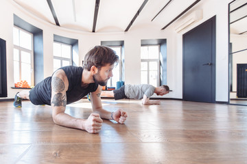 Two friends men in good physical shape doing workout together in the gym. Concept of team spirit and joint visits to the hall for support. Side view of two young sportman in sportswear doing plank