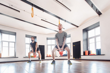Obraz premium Young strong male friends train with weights in the gym equipped with the trx system. The concept of joint training and the pursuit of a common goal