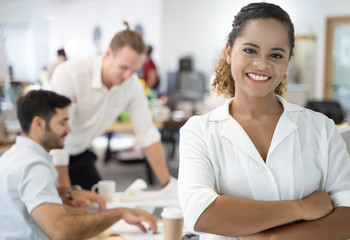 Portrait of successful young African businesswoman at office, colleagues in background.