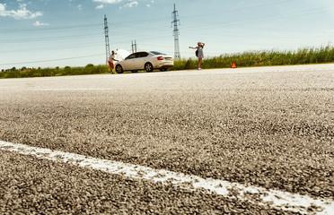 The young couple broke down the car while traveling on the way to rest. They are trying to stop other drivers and ask for help or hitchhike. Relationship, troubles on the road, vacation.