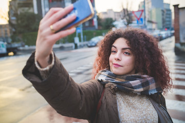 young curly woman taking selfie with smartphone