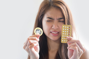 Young woman holding condom and contraceptive pills prevent pregnancy