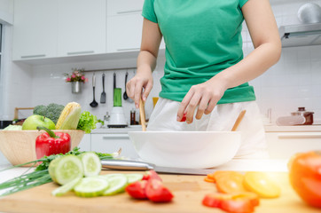 Obraz na płótnie Canvas Diet. young pretty woman in green shirt standing and preparing the vegetables salad in bowl for good healthy in modern kitchen at home, healthy lifestyle, cooking, healthy food and dieting concept