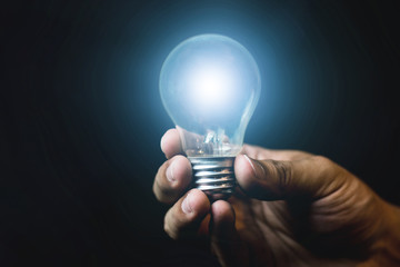 The light bulb is held in a hand that shines in blue light on a black background.concept thought