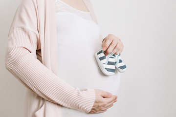 Pregnant belly with newborn baby booties close up over white background