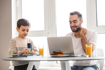Joyful bearded father and his young son having dinner