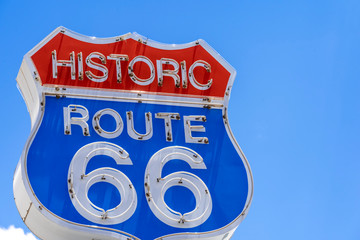 Red, white and blue neon sign on the famous, historic Route 66 in front of blue sky