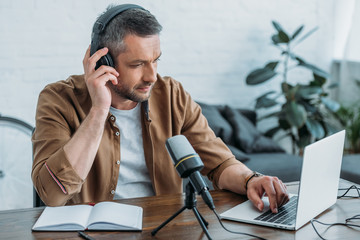 attentive radio host in headphones using laptop while sitting near microphone