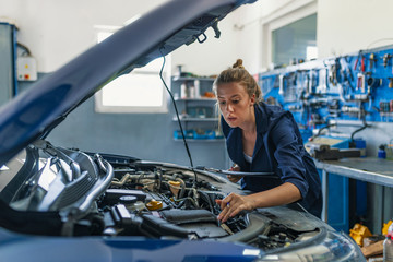 Lovely female auto mechanic smiling, examining engine of an automobile. Cheerful female car technician enjoying working at the garage, copy space. Repair, car service concept