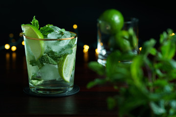 Mojito served in a glass with gold rim. Limes and mint in bokeh, dark wooden table, high resolution