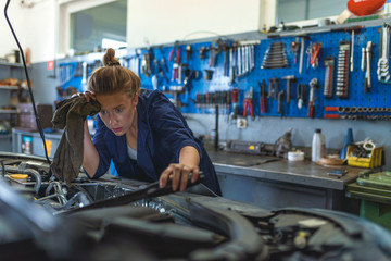 Obraz premium Female mechanic working under the hood of a car. Technician woman working in auto repair workshop. Female mechanic working on car. Repair, car service concept