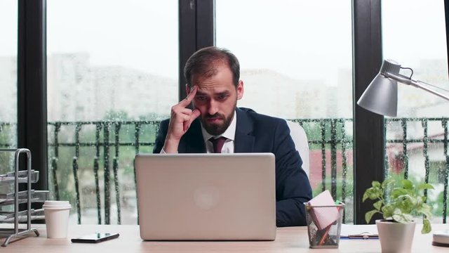 Concentrated corporate worker in business suit reads an email then disagrees and starts typing a reply. Big windows and rainy day