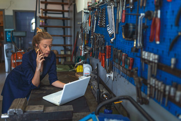 Mechanic typing on a laptop at the repair garage. Female Mechanic. Female mechanic with laptop. Young female mechanic with laptop. Craftswoman working using a laptop in the garage