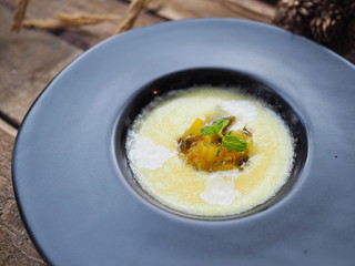 Cold refreshing sweet sour diced tropical summer pineapple cube coconut gazpacho soup with mint leave decorated on top in bowl on wooden table