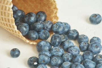 close up of waffle cone with blueberries on white concrete background with copy space