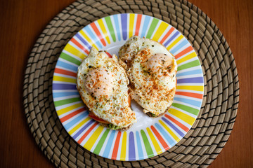 Two cereal bread slices with avocado, tomato and fried egg on top, presented on a colorful plate on a wooden table tasty breakfast