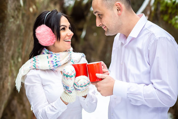 Loving couple resting and drinking morning coffee together in the mountains, rocks, snow. Winter holidays in mountains. Man and woman wearing knitted clothing having fun on weekends