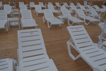white plastic lounge chairs for relaxing and sunbathing outdoors by the pool,on wooden flooring