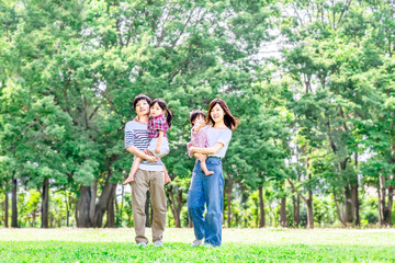 新緑の樹木をバックに公園を散歩する4人家族。育児、愛情、幸せイメージ