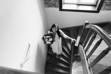 Girl is gathering for a walk. Husband is waiting for wife. Female is preparing for a date. Dressing a newly-married couple. Woman in white dress holding bouquet on a stairs