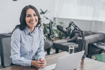 smiling radio host sitting at workplace near microphone and looking at camera